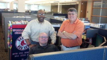 Andre Mooney and Numa Gomez (standing, from left) with Bob Greene in his Red Sox-centric cubicle.