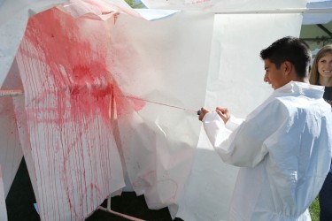 A student spurts fake blood  onto a blank canvass as part of a blood-spatter analysis demonstration at GCU's Forensic Science Day.