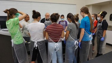 Students in the Medical, Engineering and Technical (MET) Professional Academy listen as Dr. Richard Holzer, a GCU faculty adjunct professor and MET biology teacher, teaches them about the cadaver in front of them. 
